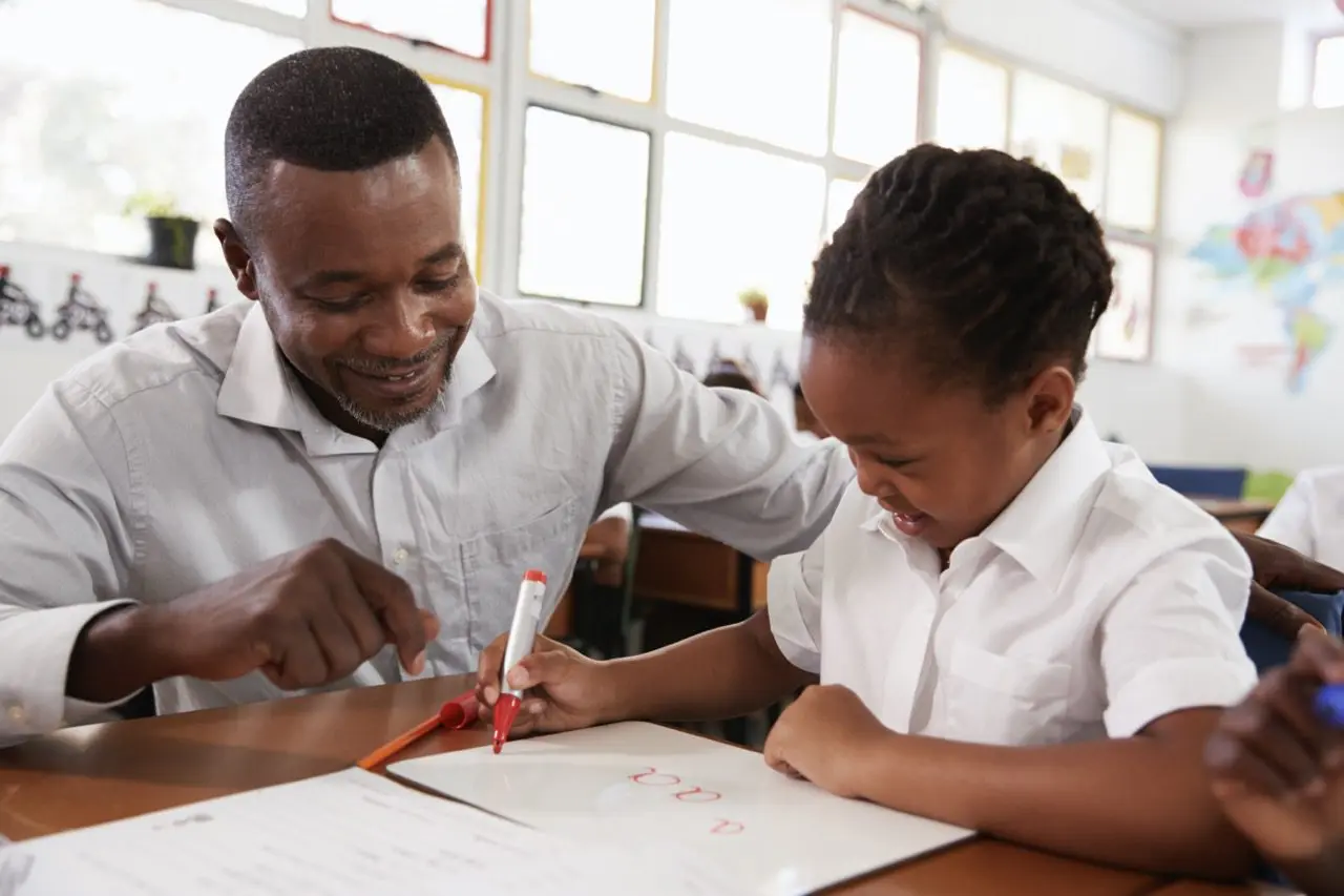 teacher helping elementary school girl at her desk 2024 10 19 13 10 10 utc Large